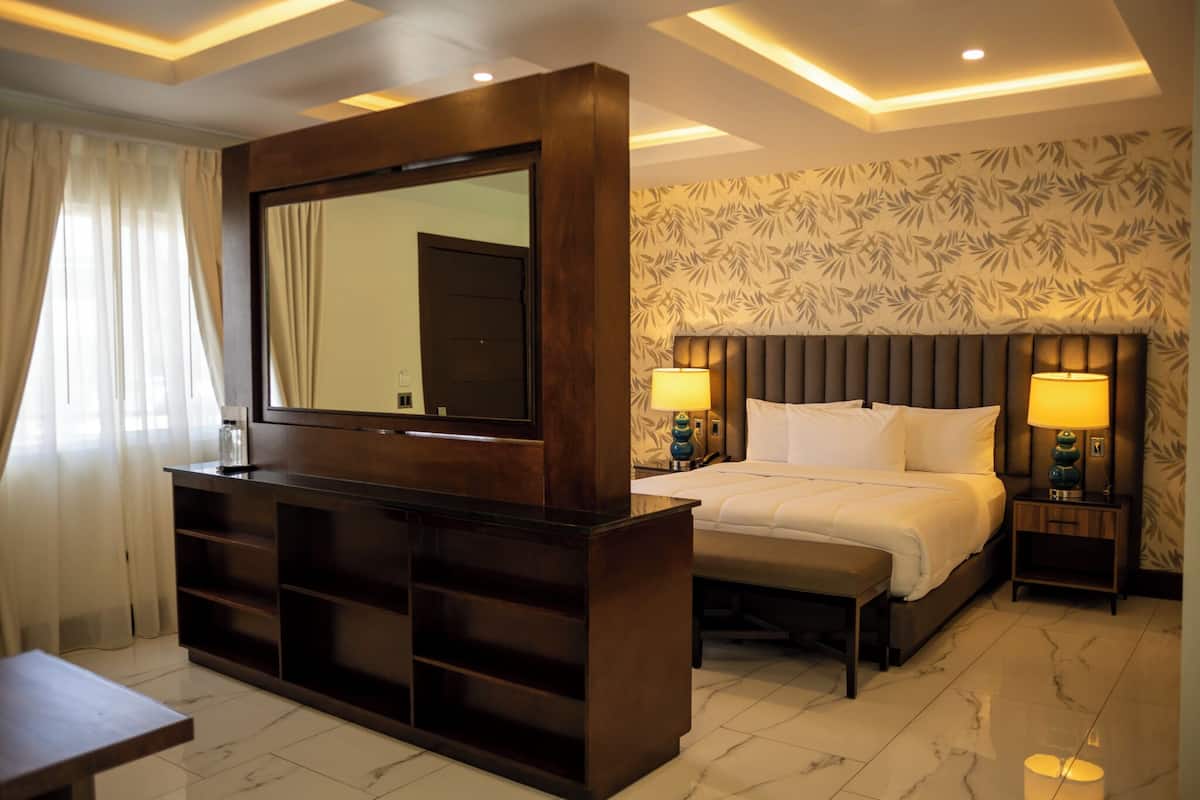 Habitación de hotel con un espejo grande, una cama con dos almohadas, una mesita de noche y un velador con lámpara.