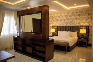Habitación de hotel con un espejo grande, una cama con dos almohadas, una mesita de noche y un velador con lámpara.