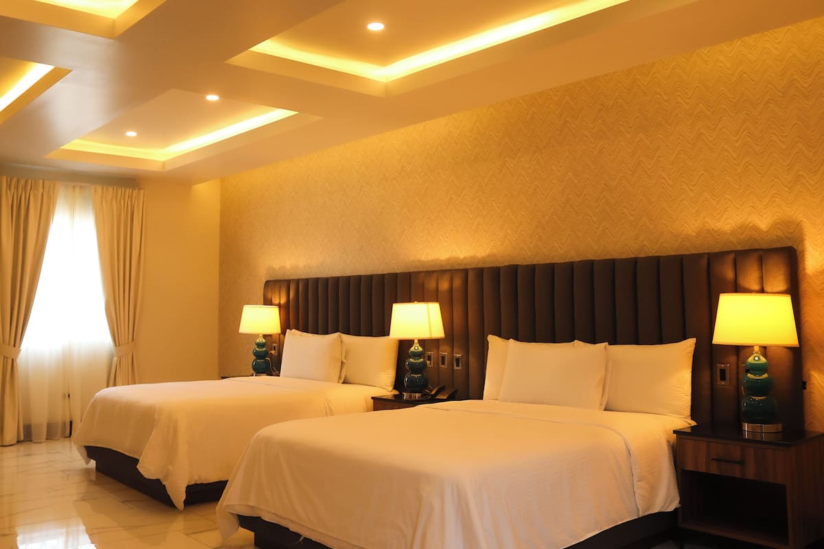 Habitación de hotel con dos camas, un cabecero grande y una mesita de noche con lámparas.