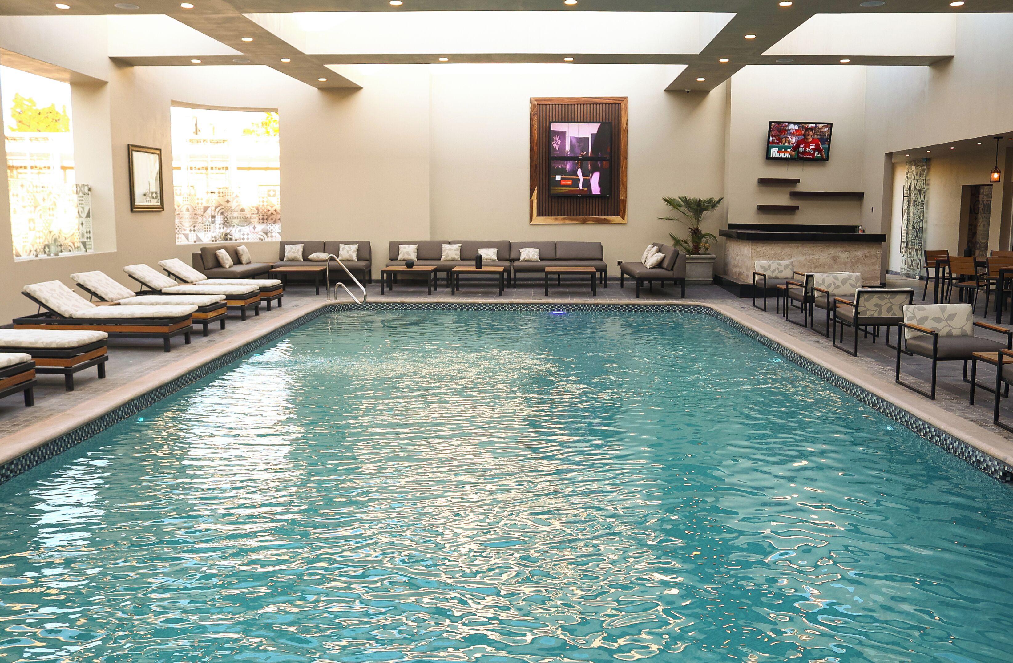A swimming pool with lounge chairs and a television mounted on the wall.