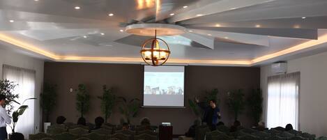 A conference room with a presentation screen, a speaker, and rows of chairs.