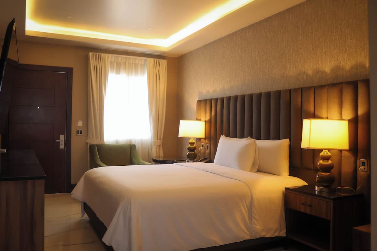 Habitación de hotel con una cama grande, dos lámparas de noche, un cabecero de madera, una silla verde y un escritorio de madera.