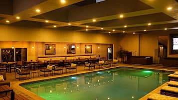 Ein Poolbereich mit Liegestühlen und Tischen, eine Bar mit Sitzgelegenheiten und eine Treppe zu einer erhöhten Ebene.