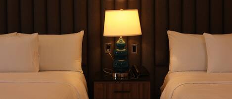 A hotel room with two beds, a nightstand with a lamp, and a telephone.