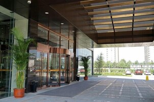 Una entrada moderna de edificio con puertas de cristal, plantas en macetas y un área cubierta.