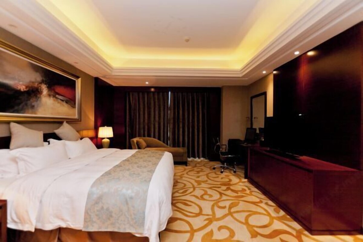A hotel room with a large bed, a desk, a television, and a red accent wall.