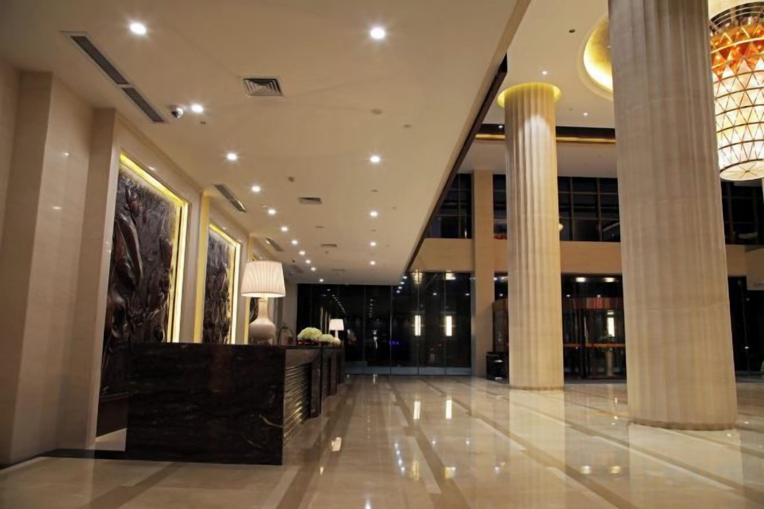 A hotel lobby with a reception desk, large columns, and a modern chandelier.