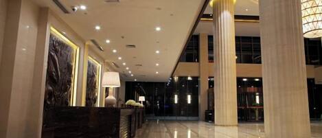 A hotel lobby with a reception desk, large columns, and a modern chandelier.
