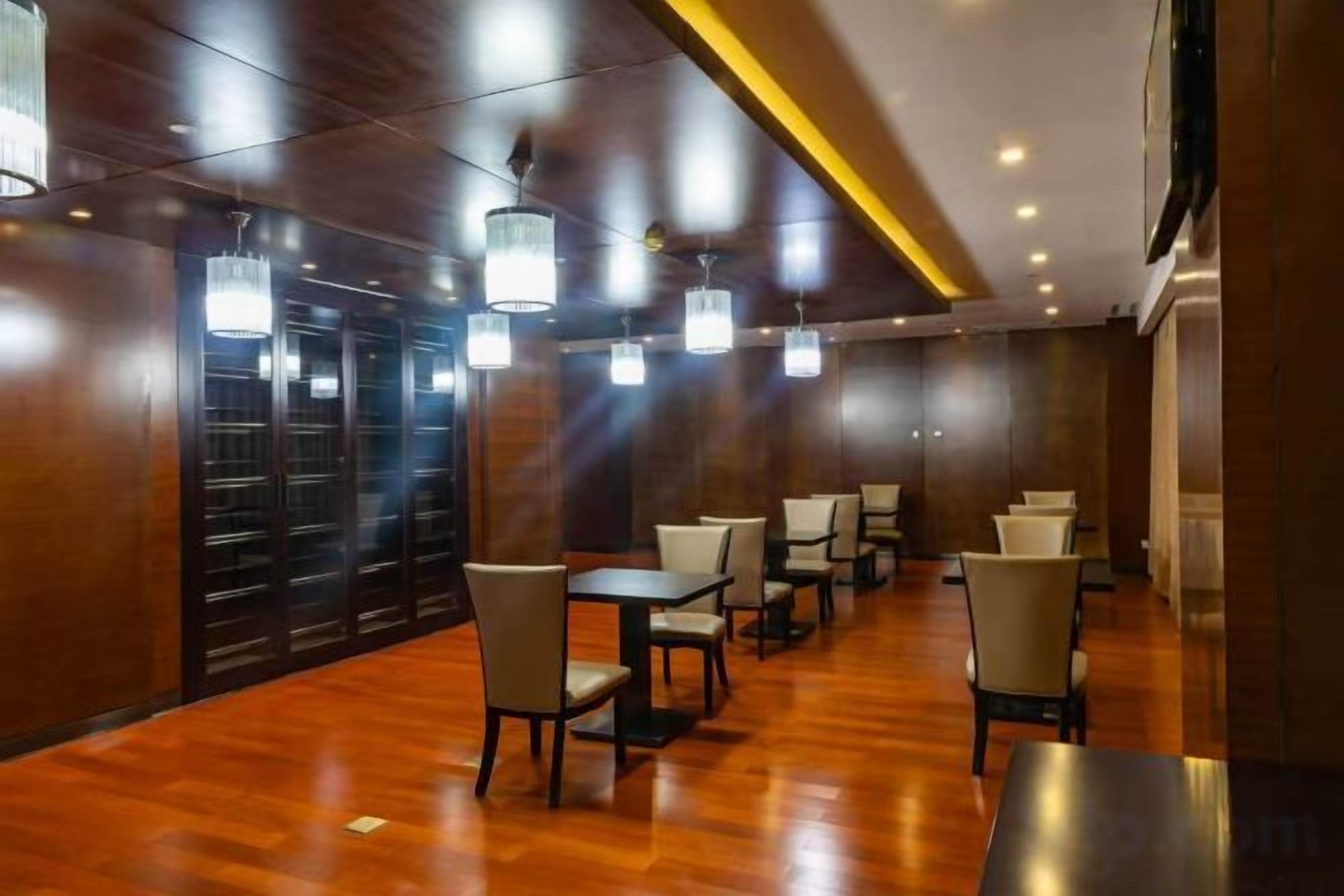 A hotel lobby with wooden flooring, multiple tables and chairs, and pendant lighting.