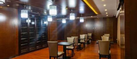Vestíbulo de hotel con suelo de madera, varias mesas y sillas, e iluminación colgante.