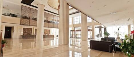 A spacious lobby with a high ceiling, large windows, and a reception desk.