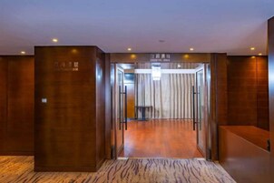 Vestíbulo de hotel con mostrador de recepción, puerta de cristal de entrada y alfombra estampada.