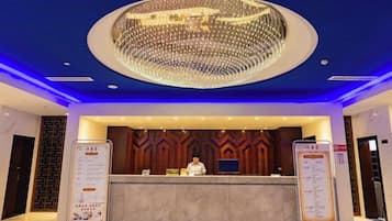 A hotel reception area with a modern design, featuring a large chandelier, a reception desk, and informational stands.