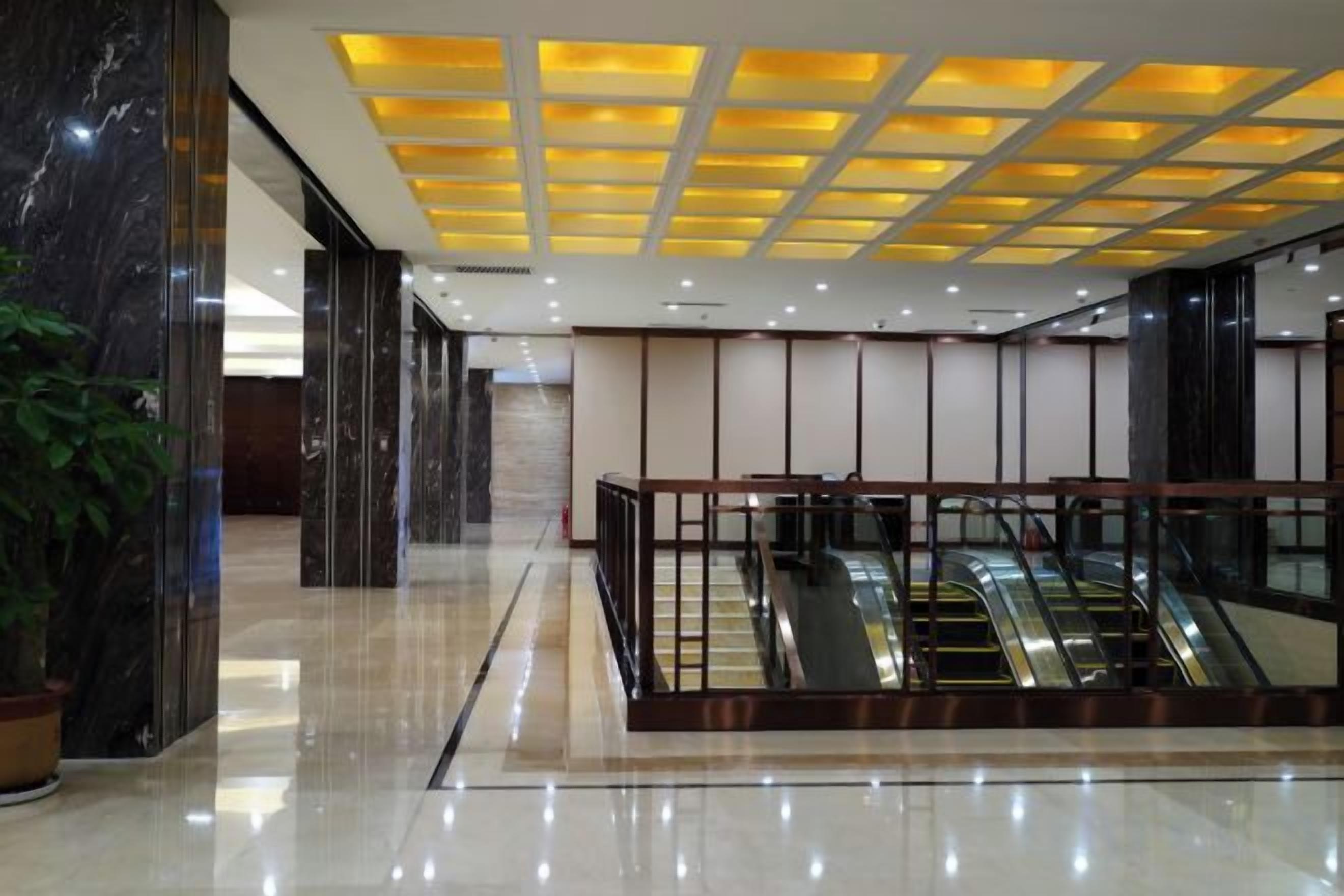 Un hall d’entrée moderne doté d’un ascenseur en verre, d’un sol en marbre et d’un plafond pourvu d’un éclairage encastré.