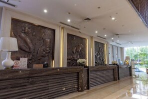 A reception area with a dark reception desk, wall-mounted sculptures, and a glass partition. - Qingcheng Hotel (Qinghe)