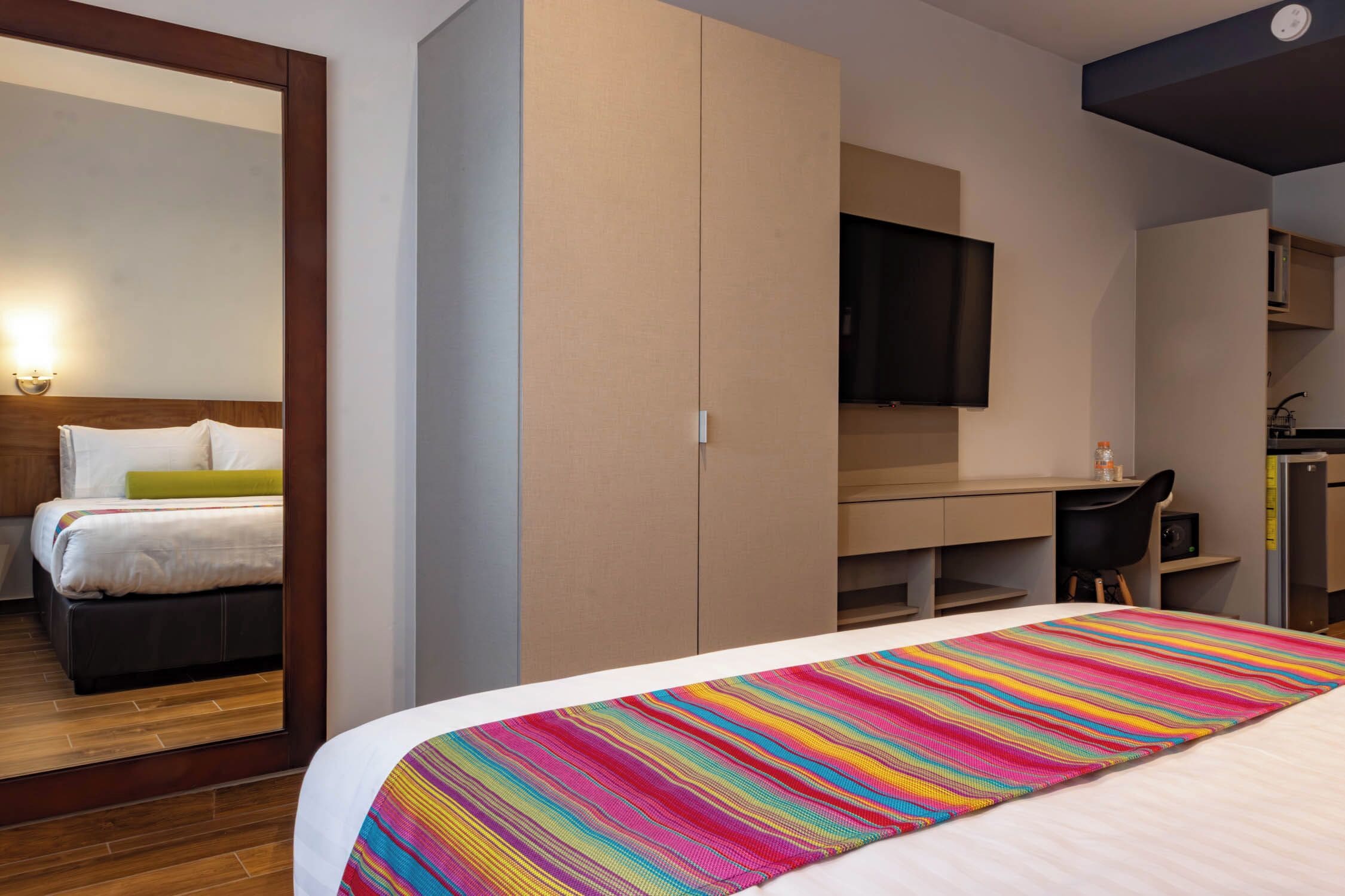 A hotel room with a bed, a desk, a chair, a television, and a wardrobe.