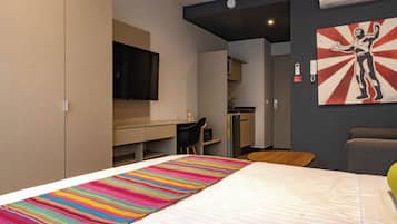 Een hotelkamer met een bed, een bureau, een stoel, een televisie en een schilderij aan de muur.