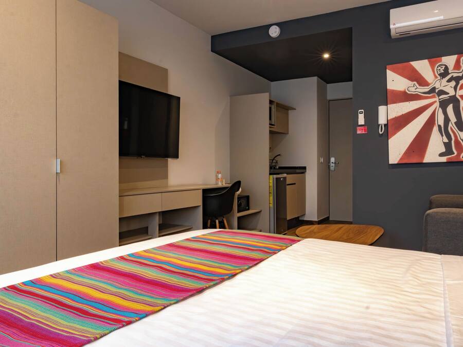Een hotelkamer met een bed, een bureau, een stoel, een televisie en een schilderij aan de muur.