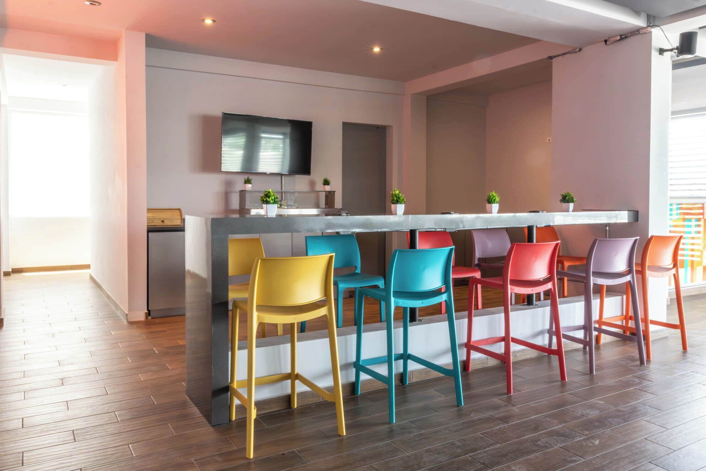 A modern kitchen with a bar area, wooden flooring, and colorful bar stools.