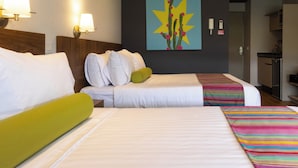 Ein Hotelzimmer mit zwei Betten, einem Bild an der Wand und einer Küchenzeile im Hintergrund.
