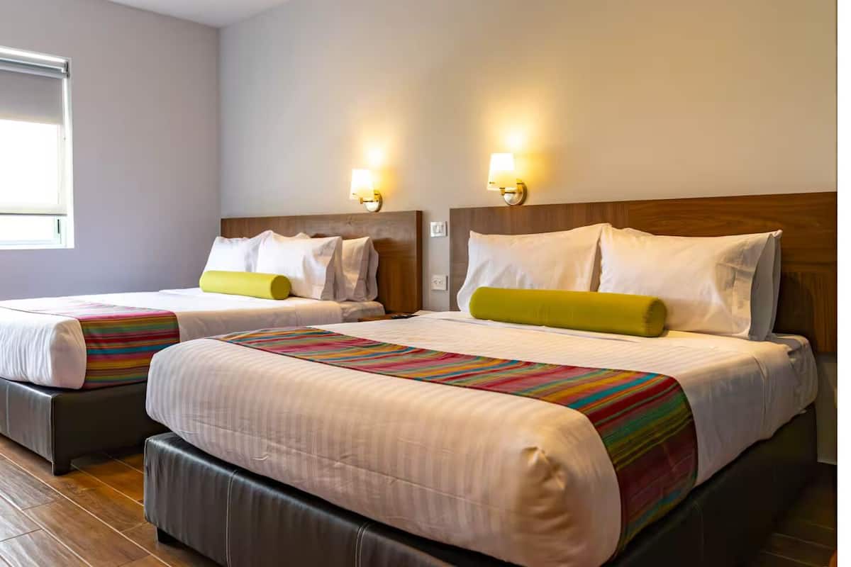 Une chambre d’hôtel avec deux lits, chacun doté d’une tête de lit, d’une fenêtre et de lampes fixées au mur.