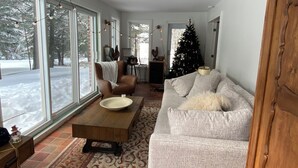 A spacious living room with large windows, a fireplace, a Christmas tree, and a cozy seating area.