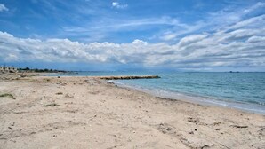 Una spiaggia sabbiosa con un molo roccioso e un mare calmo sotto un cielo parzialmente nuvoloso.