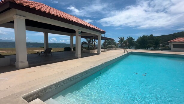 Una piscina con zona coperta, vista sul mare e cielo sereno.