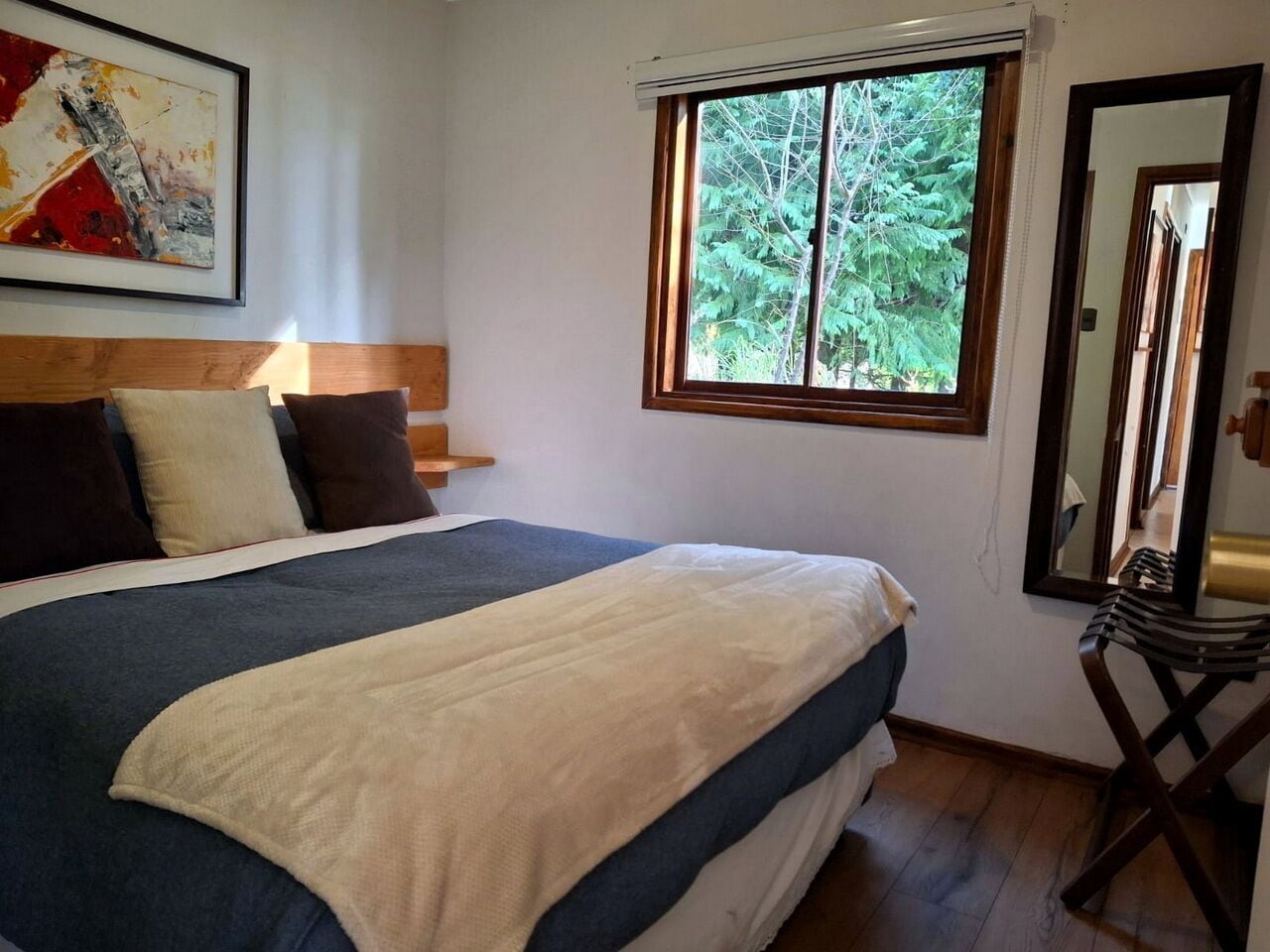 Una camera da letto con un letto grande, una finestra vista alberi, una testiera in legno e uno specchio.