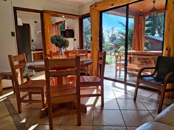 A wooden dining area with a table and chairs, a potted plant, and a view of the outdoors through large windows. - cabañasmapulauquen (Villarrica)