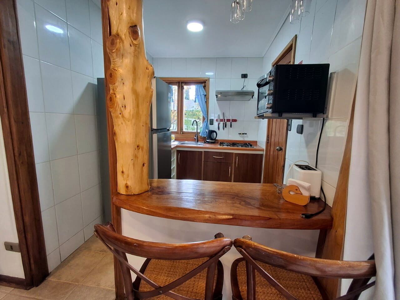 Cozinha com ilha de madeira, duas cadeiras, uma TV fixada na parede e uma janela com vista para o exterior.