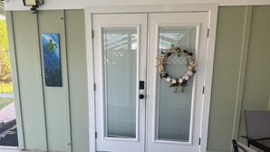 A front door with a glass panel, a doormat, a painting, and a wreath with the word "BEACH" on it.