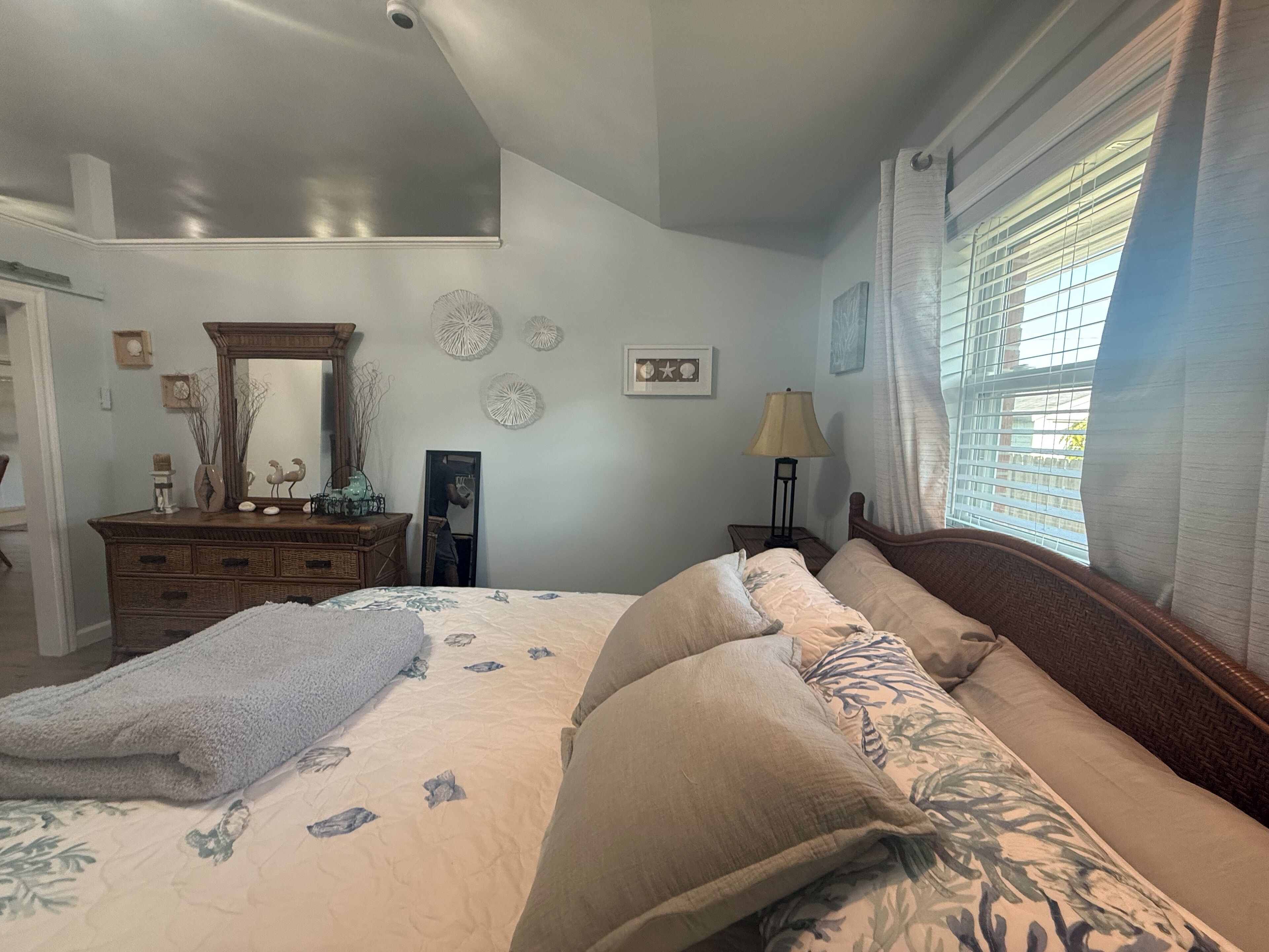 A bedroom with a bed, a dresser, a mirror, and a window with blinds.
