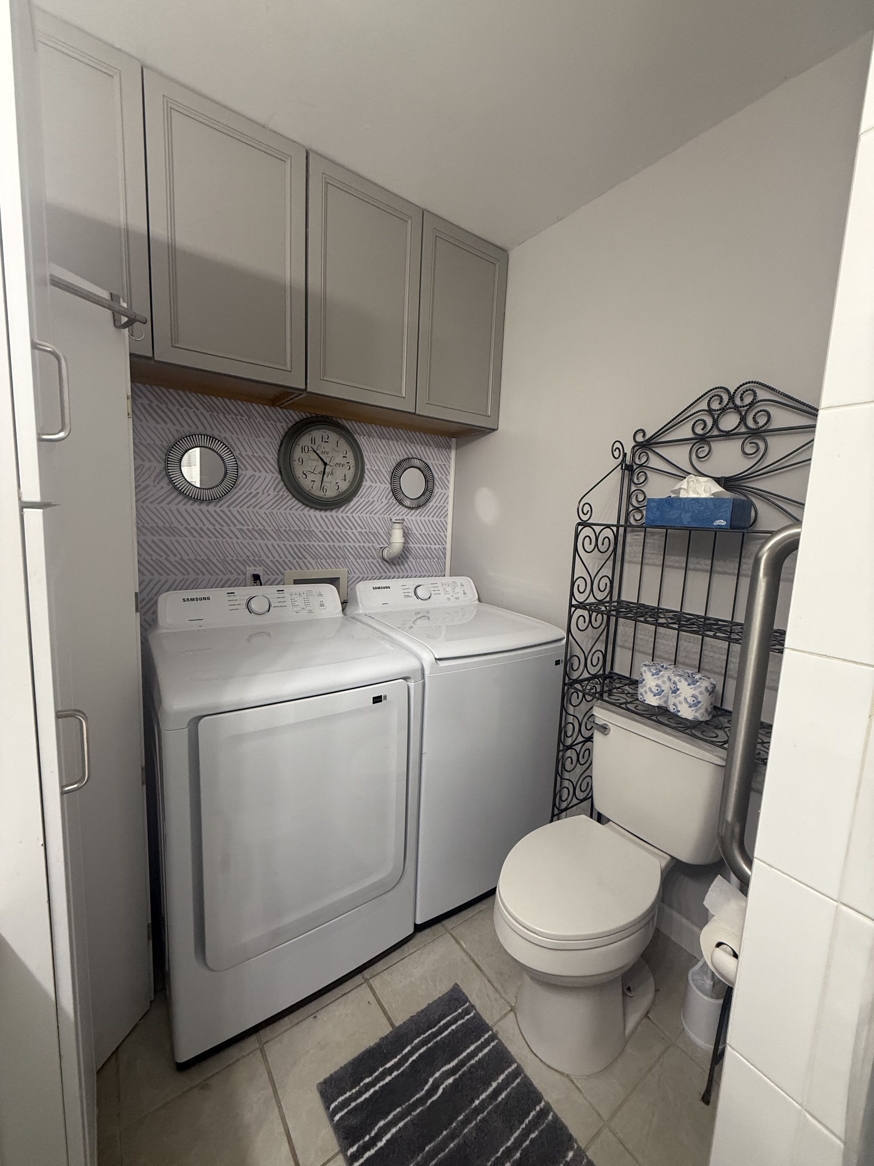 Ein kleiner Waschraum mit zwei weißen Waschmaschinen, einer Toilette und einem Metallregal mit Pflegeprodukten.