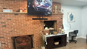 A living room with a brick fireplace, a television mounted above it, and a desk with a chair.