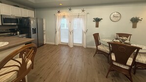 A kitchen with white cabinets, a microwave, and a refrigerator. There is a dining area with a table and chairs, and a window with curtains.