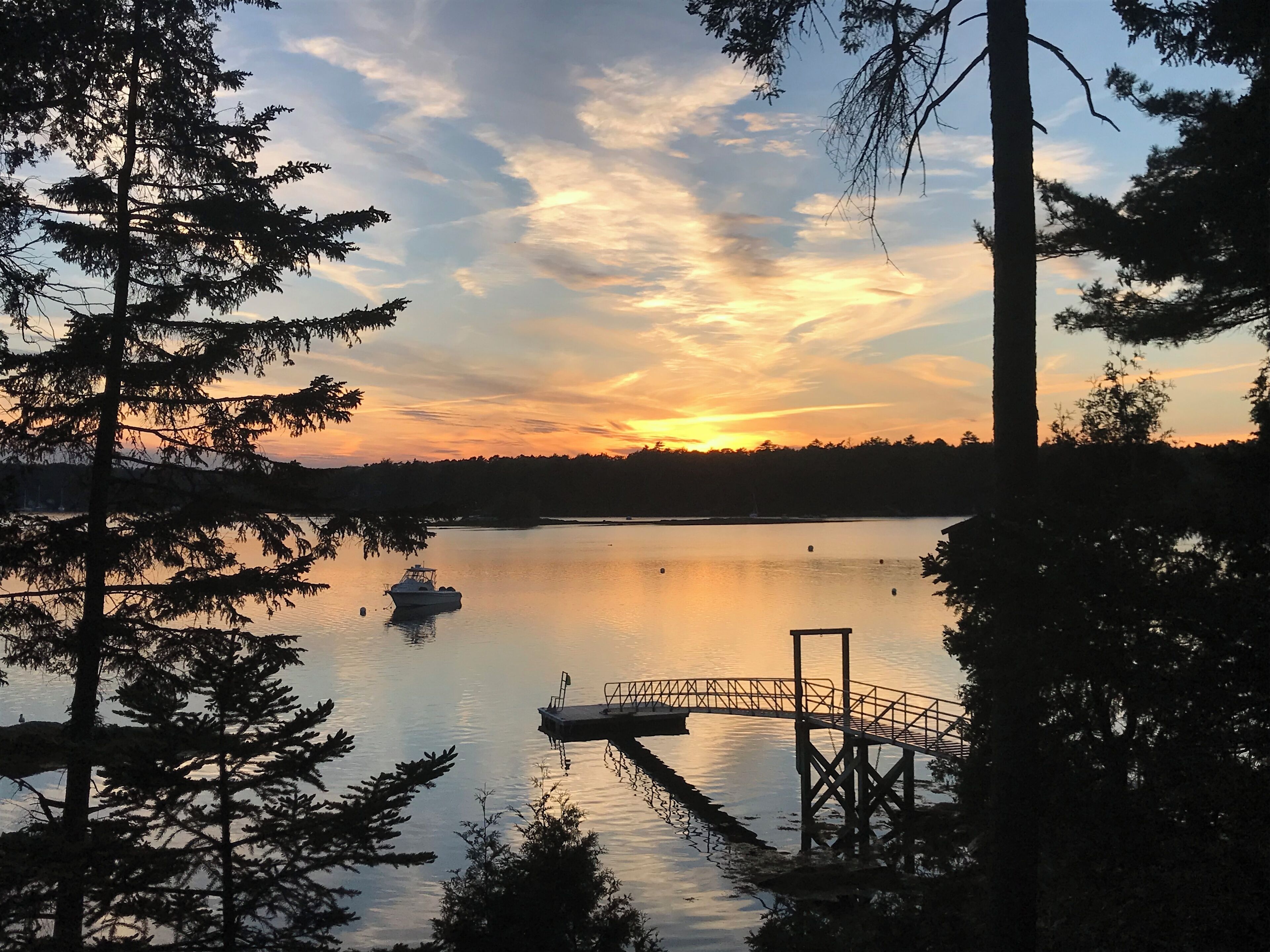 A calm lake at sunset with a dock and a boat.