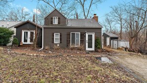 A two-story house with a front porch, a garage, and a small shed in the backyard.