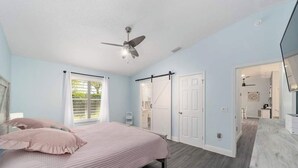 Een slaapkamer met een bed, een plafondventilator, een deur en uitzicht op een badkamer.