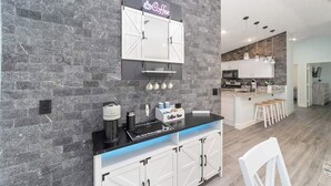 Een moderne keuken met een koffiebar, witte kastjes en een bakstenen muur.