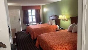 A hotel room with two beds, a desk, a chair, a lamp, and a window with curtains.
