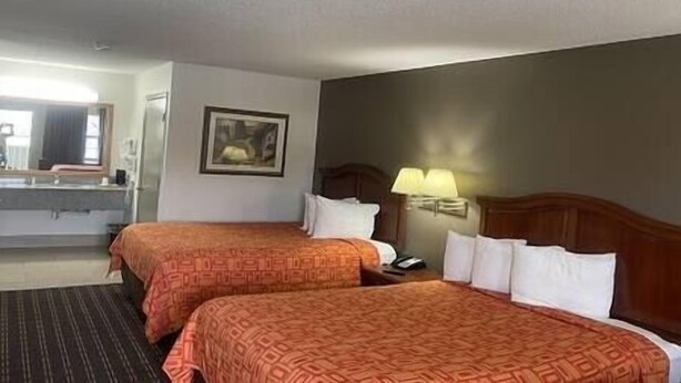 A hotel room with two beds, a desk, a chair, a lamp, and a framed picture on the wall.