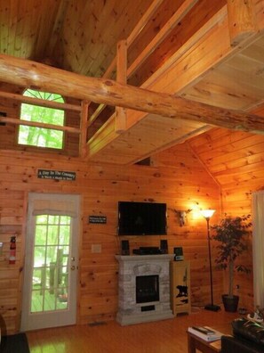 A log cabin interior with a stone fireplace, a mounted television, and a door with a window.