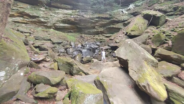 Un paysage rocheux où l’on voit une personne se tenant au milieu de gros blocs de pierre et de rochers couverts de mousse.