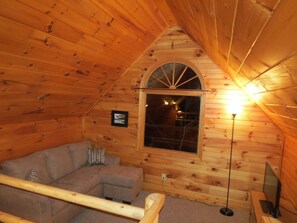 A cozy wooden cabin room with a sofa, a small table, and a lamp.