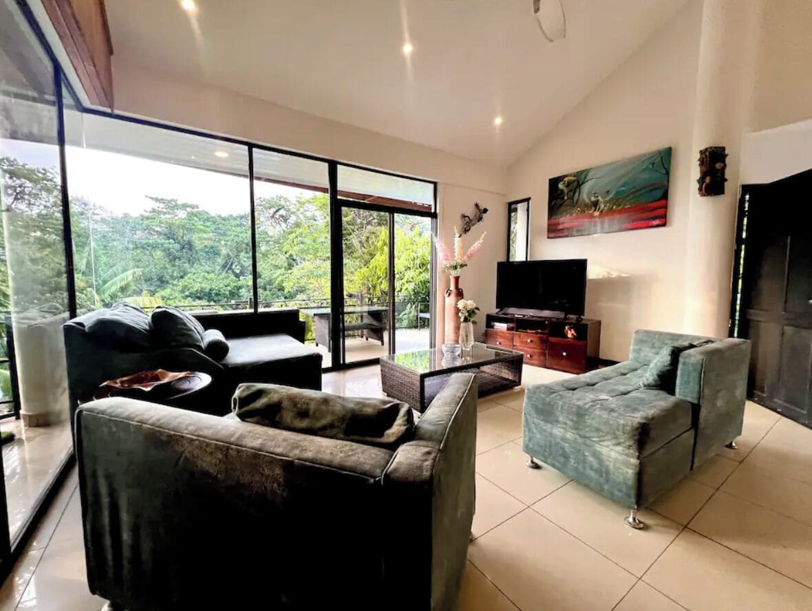 A spacious living room with a large glass door leading to a balcony, a flat-screen TV, and a painting on the wall.