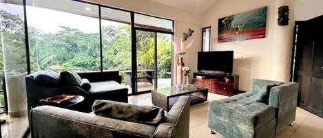 A spacious living room with a large glass door leading to a balcony, a flat-screen TV, and a painting on the wall.