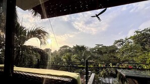 Un balcon offrant une vue sur un coucher de soleil, des palmiers et un oiseau en vol.