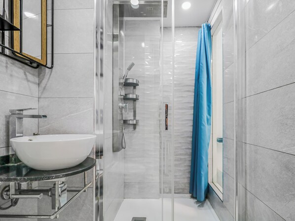 A modern bathroom with a white sink, a glass-enclosed shower, and a blue shower curtain. - Endless Seaview Patalavaca (Patalavaca)