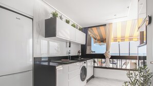 A modern kitchen with a built-in washing machine, white cabinets, and a view of the sea through a large window. - Endless Seaview Patalavaca (Patalavaca)